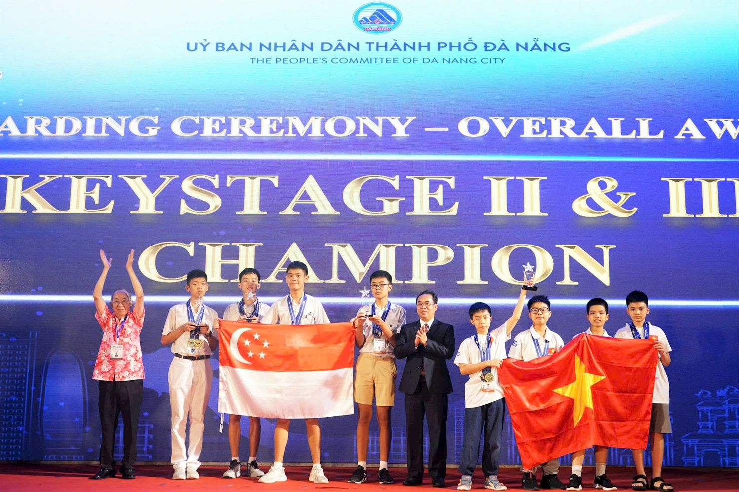 Phó Chủ tịch UBND TP. Đà Nẵng Trần Anh Tuấn (thứ 5, từ phải sang) và GS. WEN-Hsien Sun Chủ tịch Ủy ban Toán quốc tế IMC (ngoài cùng bên trái) trao giải vô địch toàn đoàn cho đoàn Việt Nam và Singapore. Ảnh: T. Huy