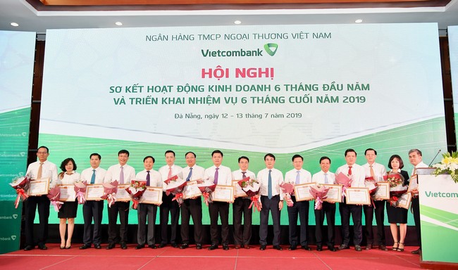 Chủ tịch HĐQT Vietcombank Nghiêm Xuân Thành (thứ 7 từ phải sang) và Tổng giám đốc Phạm Quang Dũng (thứ 6 từ trái sang) trao Giấy khen và tặng hoa cho 14 chi nhánh tiêu biểu trên một số mặt hoạt động 6 tháng đầu năm 2019