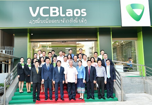 Đồng chí Trần Quốc Vượng, Ủy viên Bộ Chính trị, Thường trực Ban Bí thư (thứ 4 từ trái sang, hàng thứ nhất) chụp hình lưu niệm với Đại diện Ban lãnh đạo,  cán bộ nhân viên Vietcombank trước Trụ sở Vietcombank Lào tại Viên Chăn.