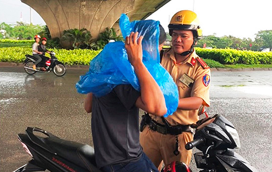 Chiến sĩ thuộc Đội CSGT Tân Túc, CA TP Hồ Chí Minh phát áo mưa miễn phí cho người lưu thông ở gầm cầu vượt Nguyễn Văn Linh.