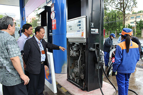 Cán bộ Cục Thuế tỉnh Lâm Đồng (đứng giữa) kiểm tra việc dán tem đồng hồ cột bơm xăng để chống thất thu đối với hoạt động kinh doanh xăng dầu